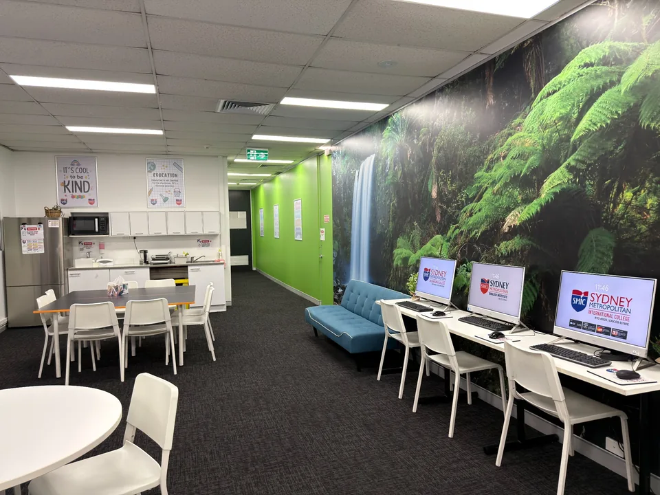 Campus learning area with computers, tables, a sofa and a green landscape wall mural