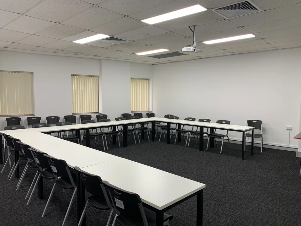 Campus teaching room with tables and black chairs arranged around an open centre
