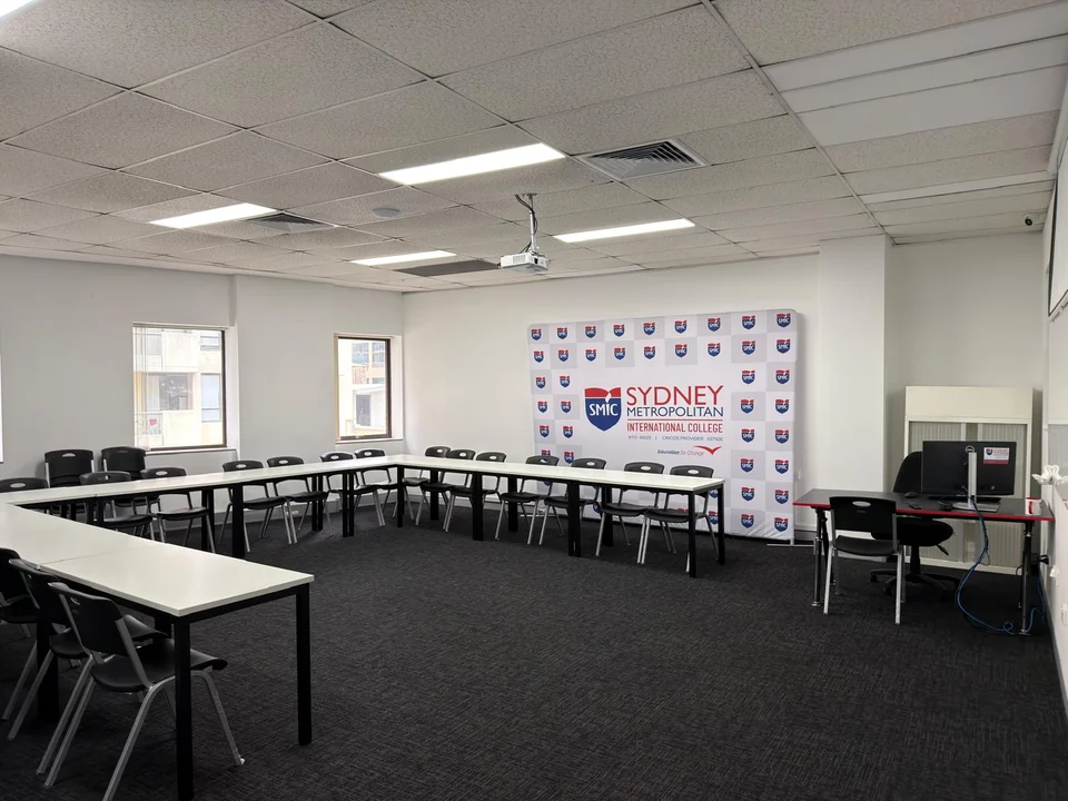SMIC training room with U-shaped tables, black chairs, projector and college backdrop